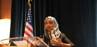 Woman speaking at podium with American flag background.