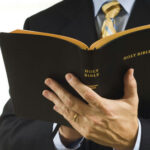 Tiny Clause Change IGNITES Nationwide Protests… Man in suit holding an open Holy Bible.