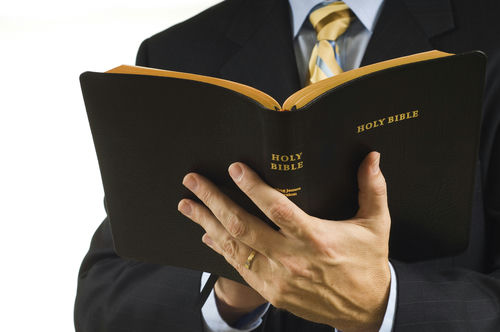 shutterstock_10073746.jpg Man in suit holding an open Holy Bible.