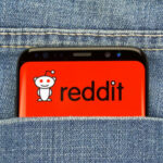 HUNDREDS Subpoenaed for Criticizing ICE Online… Phone displaying Reddit logo in pocket of blue jeans.