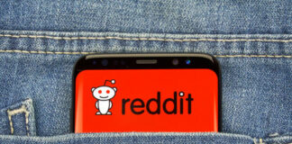 Phone displaying Reddit logo in pocket of blue jeans.