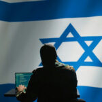BETRAYED: Israel Attack Strategy Exposed Online… Hacker in front of Israeli flag with laptop.