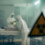 Ebola Travel BAN – Is THIS The Real Reason? Two scientists examining a patient with biohazard sign visible.