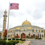 HEROIC Guard’s Death: The UNTOLD Sacrifice A mosque with a golden dome and minarets, featuring an American flag in front