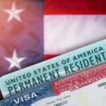 White Refugee Shocker Sparks Global BRAWL… Green card and visa with U.S. flag background.
