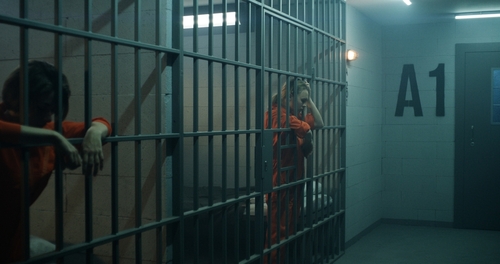 Two inmates in orange jumpsuits inside a prison cell