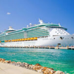 HORRIFYING Disney Worker Bust—Then They VANISHED… Large cruise ship docked near turquoise water and foliage.