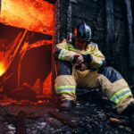 Firefighter resting near a burned-out building.