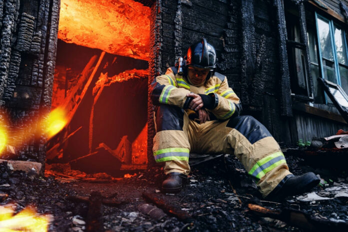 2414547803 Firefighter resting near a burned-out building.