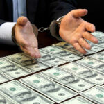 Trust Fund MURDER TWIST Stuns Court Handcuffed hands over a table of hundred-dollar bills.
