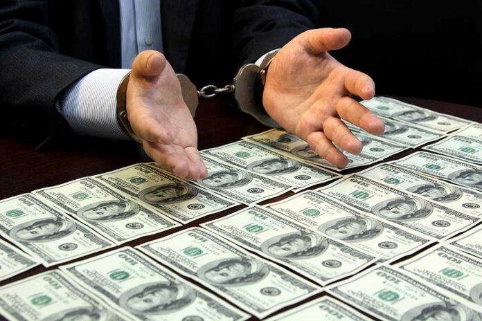 292760255 Handcuffed hands over a table of hundred-dollar bills.