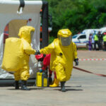11 DEAD, River Tainted — Still No Answers.. Hazmat-suited workers exit a decontamination tent