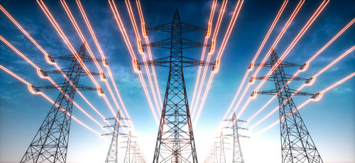 High-voltage transmission towers with glowing power lines at dusk