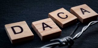 Wood letter tiles spelling DACA beside barbed wire on dark surface