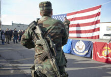 Military Uproar: Congress Debates Marijuana Waivers Soldier stands with rifle in front of American flag.