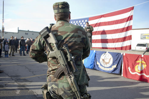 shutterstock_125334188 Soldier stands with rifle in front of American flag.