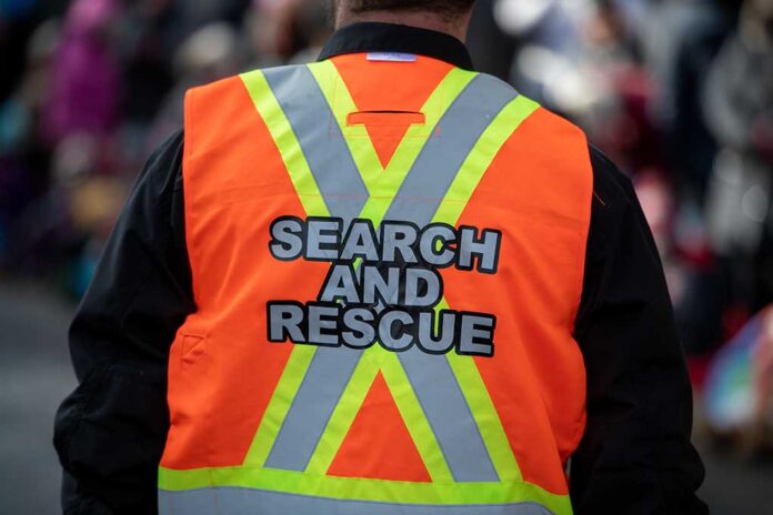 A,Male,Adult,Stands,Among,A,Crowd,With,A,Bright Search and rescue worker in an orange reflective vest seen from behind