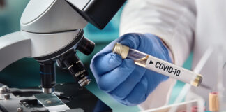 Scientist holding a test tube labeled COVID-19 next to a microscope