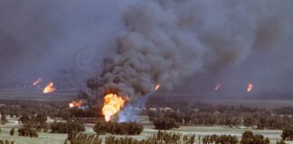 A large oil fire producing thick smoke and flames in a rural landscape