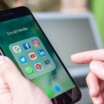 Google Sounds ALARM: Canada’s INSIDIOUS Backdoor Play Person holding smartphone with social media app folder open