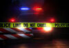 Police car behind yellow caution tape at night.