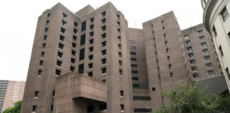 Tall concrete building with numerous windows and adjacent parked cars.