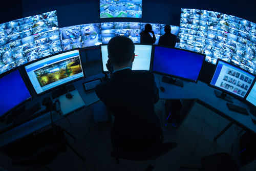 shutterstock_1047388429 Surveillance control room with multiple monitors and operators.