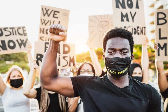 shutterstock_1762143443 Protester wearing mask raises fist during demonstration