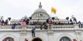 Crowd at U.S. Capitol building with flags and cameras.