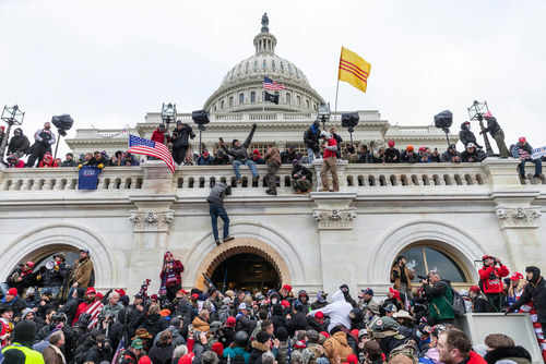 shutterstock_1889190784-1 Crowd at U.S. Capitol building with flags and cameras.