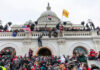 Crowd at U.S. Capitol building with flags and cameras.