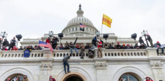 Crowd at U.S. Capitol building with flags and cameras.