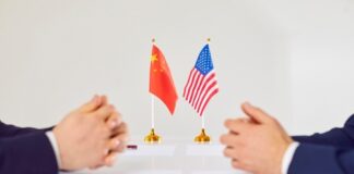 Two hands of individuals facing each other with flags of China and the USA on the table