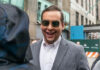 Man in sunglasses smiling on a city street.