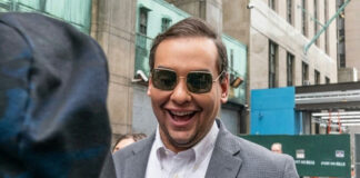 Man in sunglasses smiling on a city street.