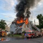 A house engulfed in flames with firefighters responding