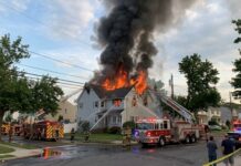 A house engulfed in flames with firefighters responding