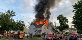 A house engulfed in flames with firefighters responding