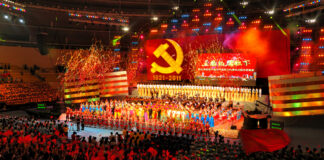 A large crowd at a celebratory event with performers on stage and fireworks in the background