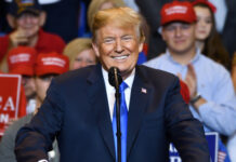 A man speaking at rally with supporters in background.