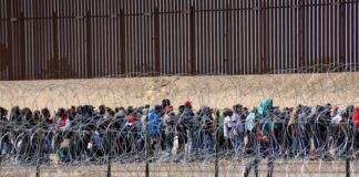 Large group of people behind barbed wire fence.