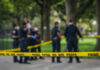 Police officers behind yellow crime scene tape in park.