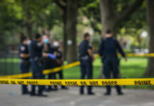 Police officers behind yellow crime scene tape in park.